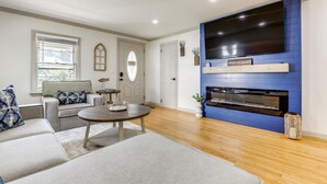 Un salon avec un canapé gris, une table basse ronde, un téléviseur à écran plat fixé à un mur bleu et une cheminée.