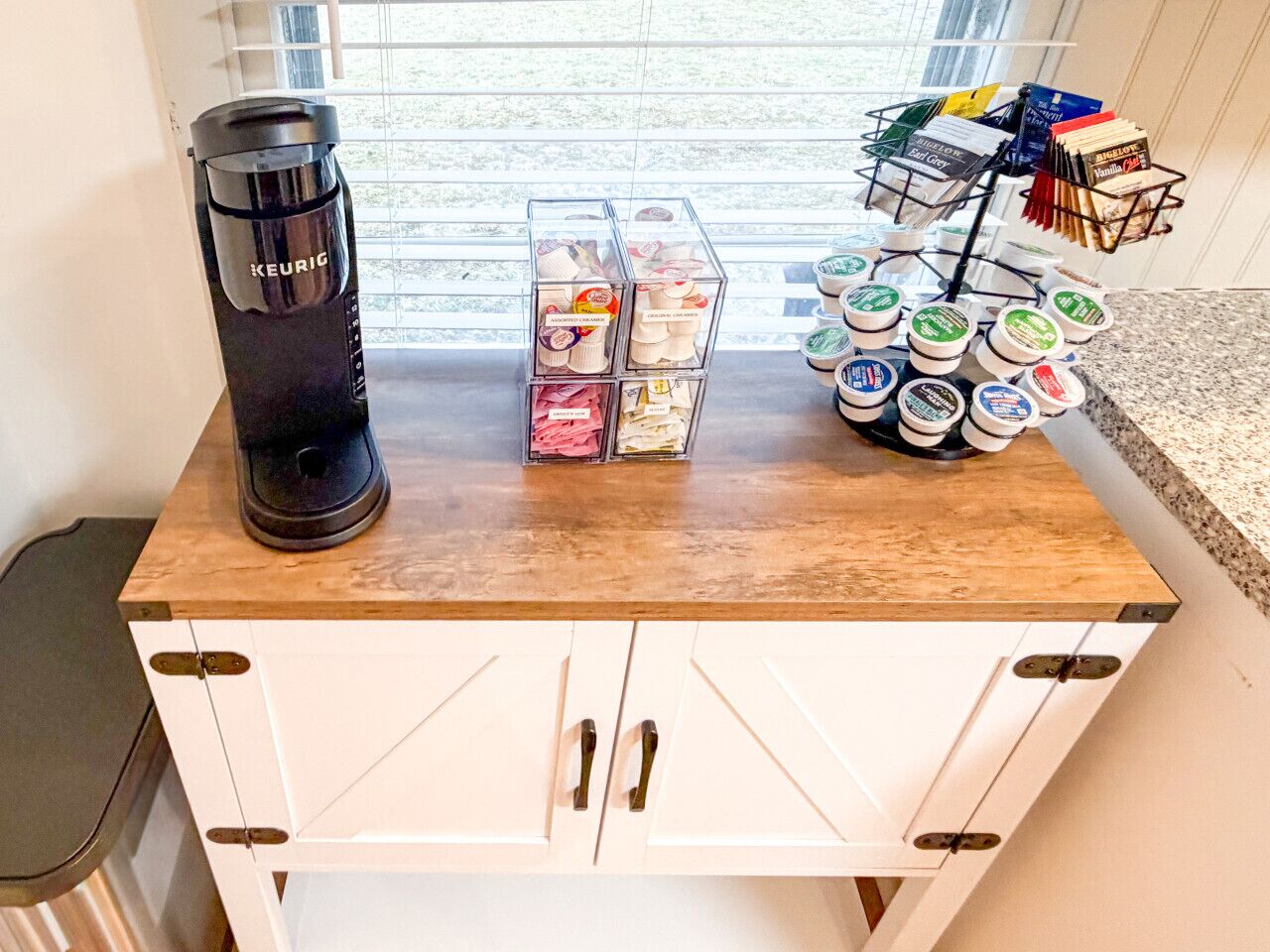 Un comptoir de cuisine avec une machine à café Keurig, un ensemble de boîtes de rangement transparentes et un présentoir à dosettes de café.