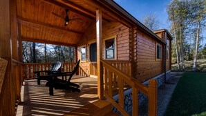 Eine Holzhütte mit Veranda, einer Bank und Blick auf den umliegenden Wald.