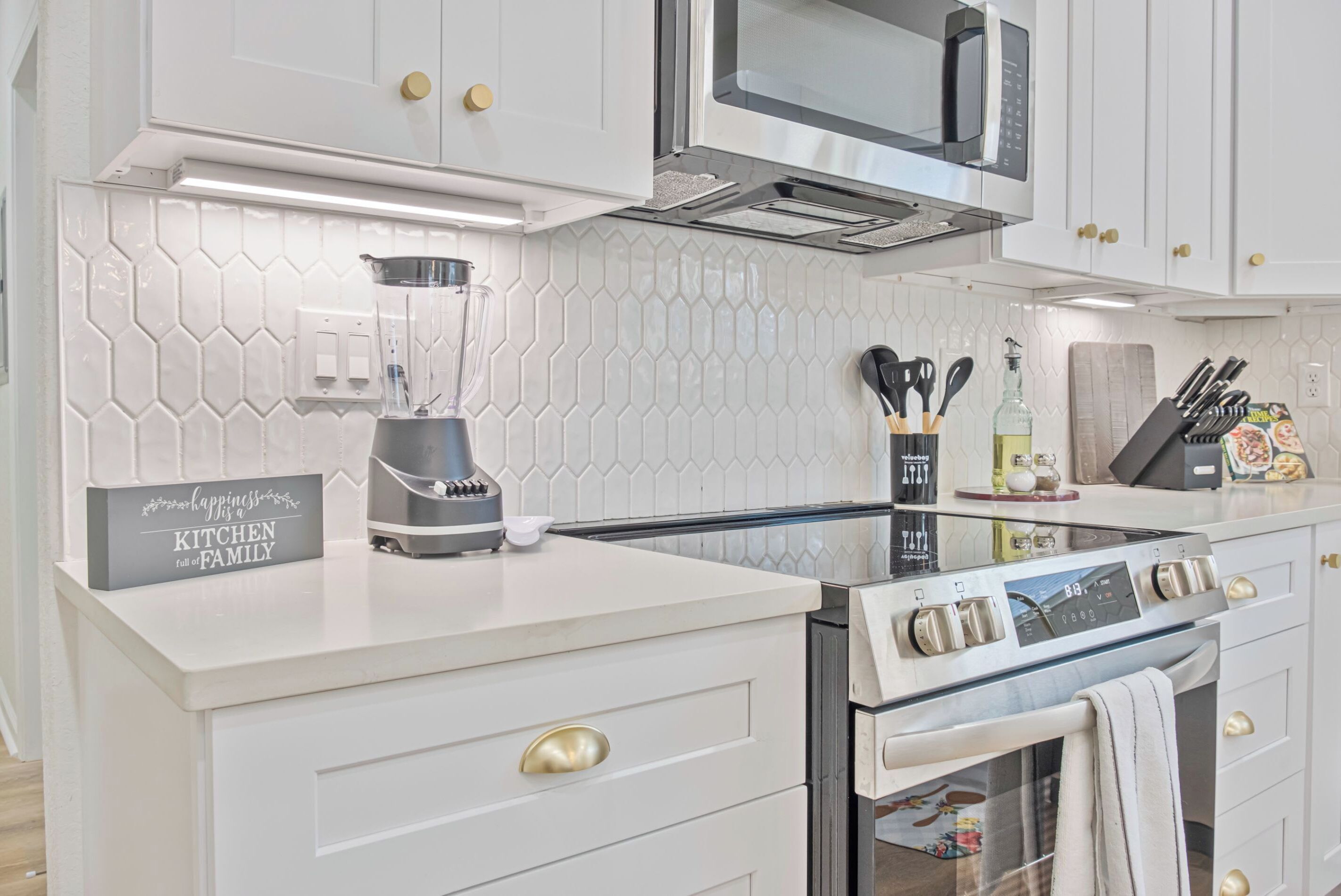A modern kitchen with white cabinetry, a built-in microwave, a stainless steel oven, and a blender on the counter.