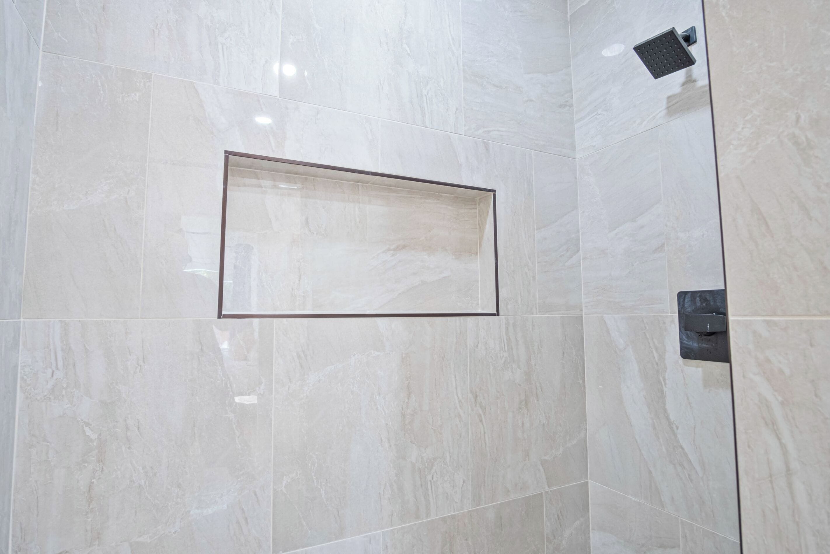 A bathroom with a shower area, a framed mirror, and a wall-mounted control panel.