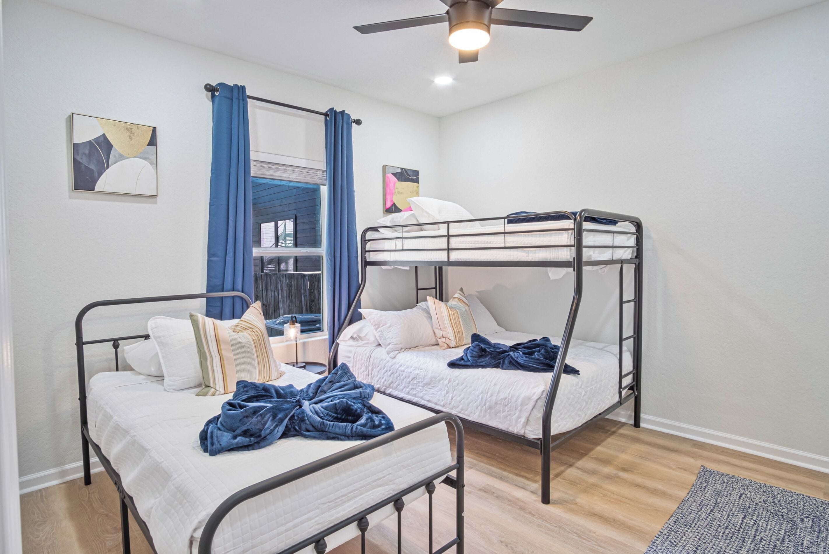 Una habitación con dos literas, un ventilador de techo y una ventana con cortinas azules.