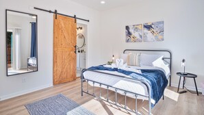 A modern bedroom with a metal bed frame, a wooden sliding door, a large mirror, and abstract wall art. - Perfect Spot to Relax 4br/3ba Near Dtown Hemisfair (San Antonio)