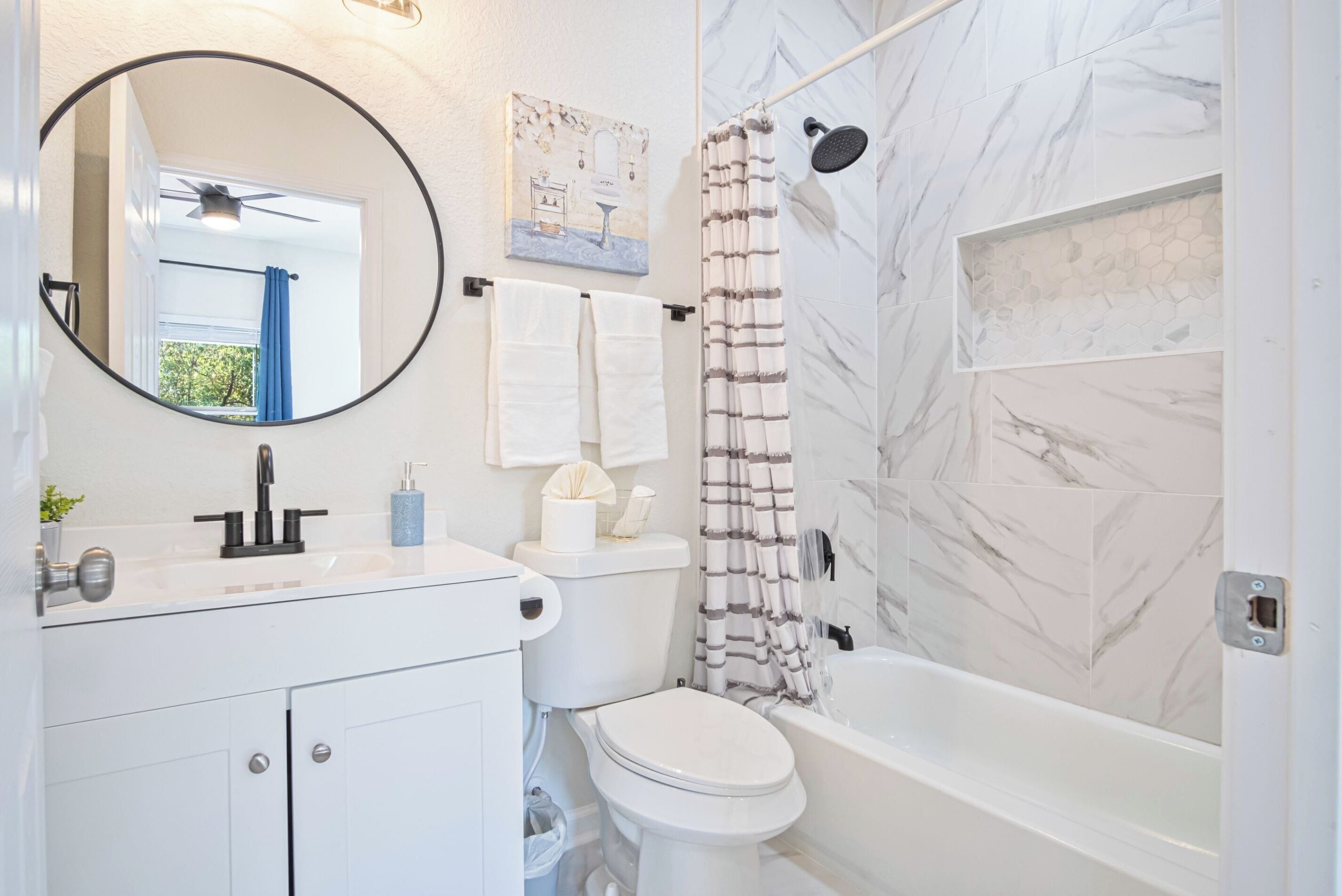Une salle de bain comprenant des toilettes, un lavabo, un miroir, un rideau de douche et un espace de douche carrelé en marbre.