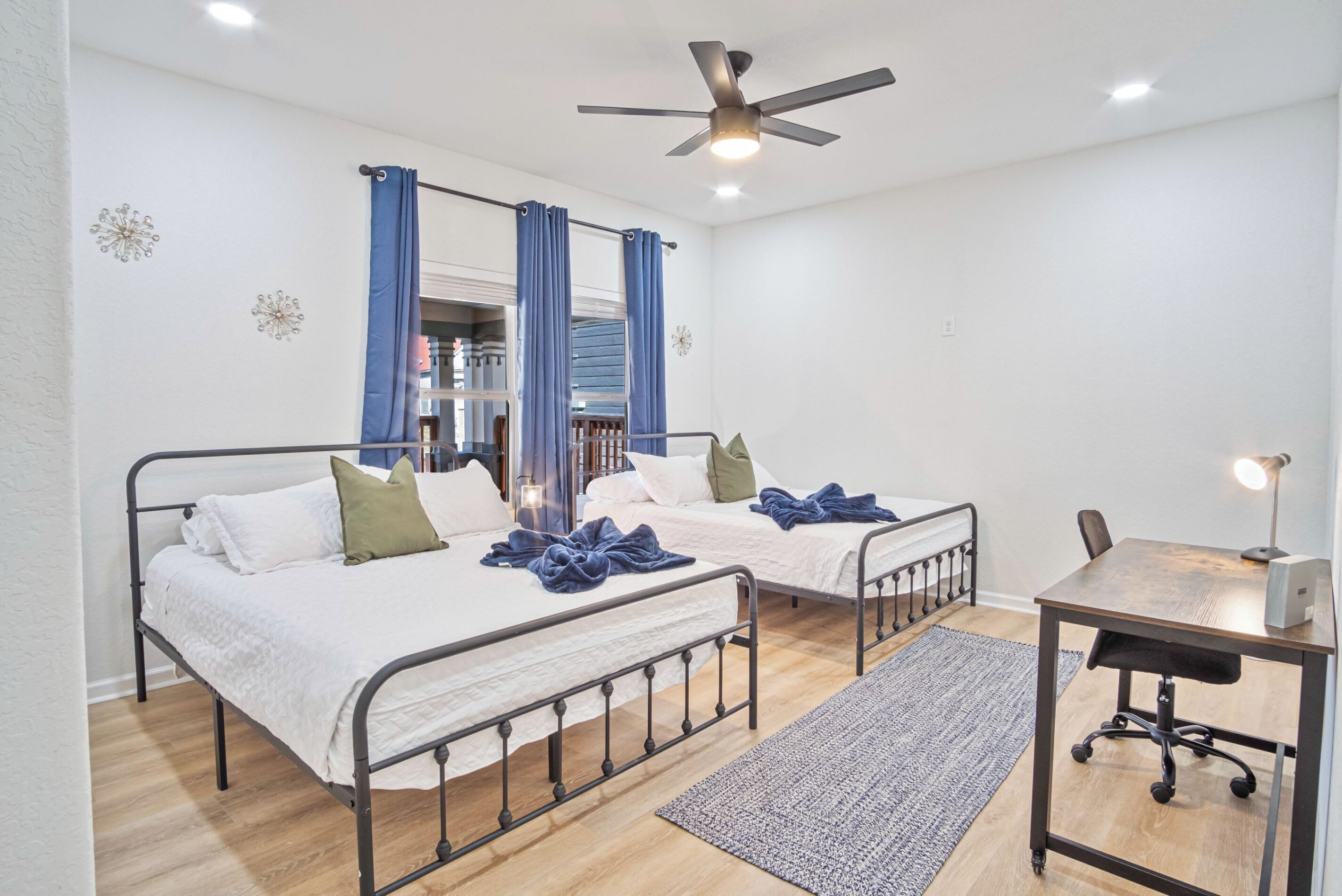 A bedroom with two beds, a desk, and a ceiling fan.
