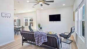 A modern living room with a ceiling fan, a flat-screen TV, and a dining area in the background. - Perfect Spot to Relax 4br/3ba Near Dtown Hemisfair (San Antonio)