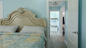 A bedroom with a bed, a white door, and a hallway leading to a balcony. - Charming Home with Beautiful Backyard near Downtown  (Fort Myers)