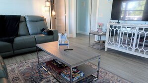 A living room with a sofa, coffee table, and a TV stand. - Charming Home with Beautiful Backyard near Downtown  (Fort Myers)