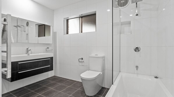 A modern bathroom with a white sink, mirror, and toilet, a shower area, and dark tiled flooring.