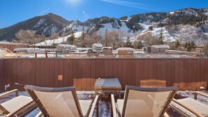 A rooftop terrace with a view of snow-covered mountains, a wooden fence, and outdoor seating. - 2-Bedroom Top Floor View Condo in Downtown Aspen (Aspen)