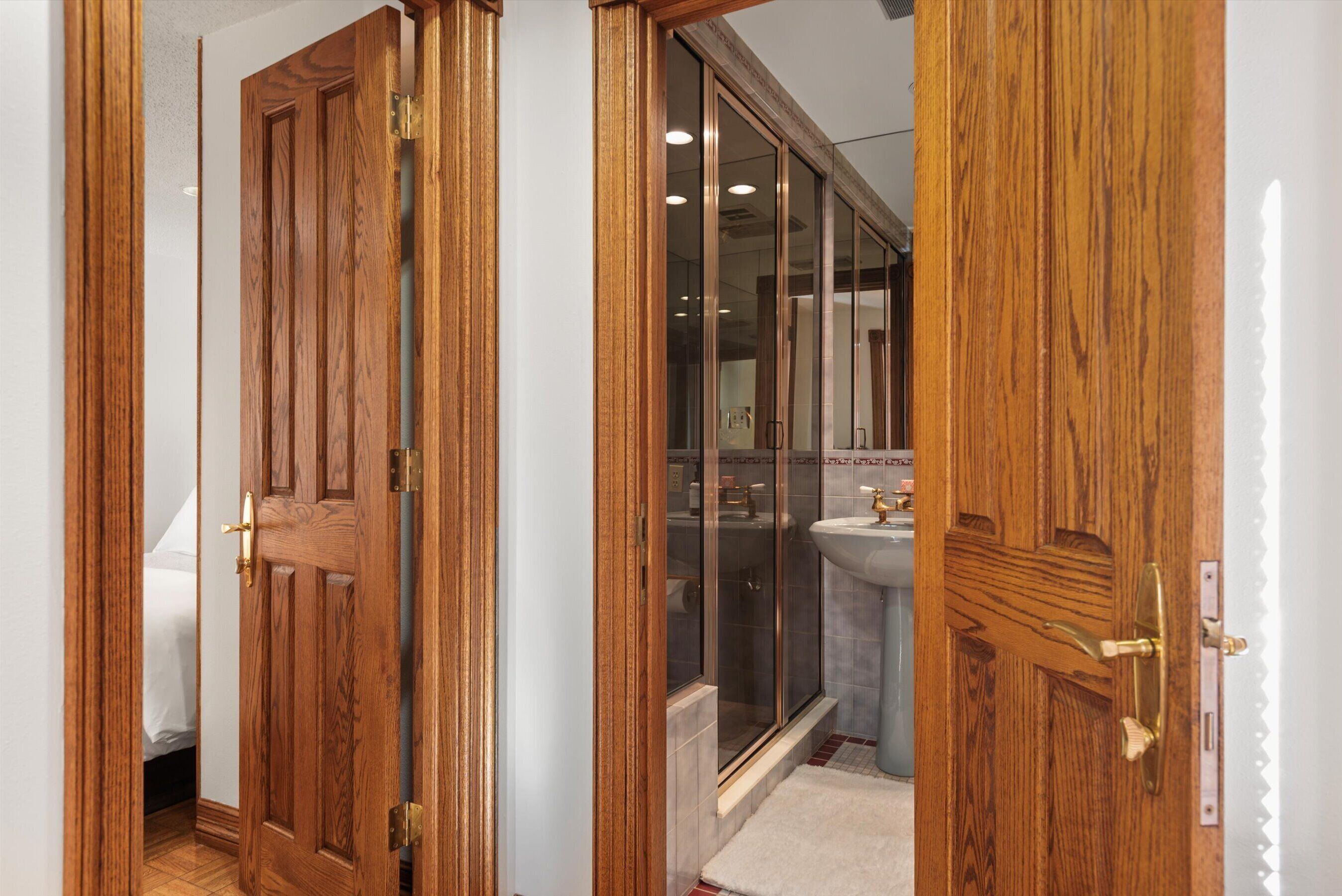 Una puerta de madera que da a un baño con cabina de ducha de vidrio y un lavabo.