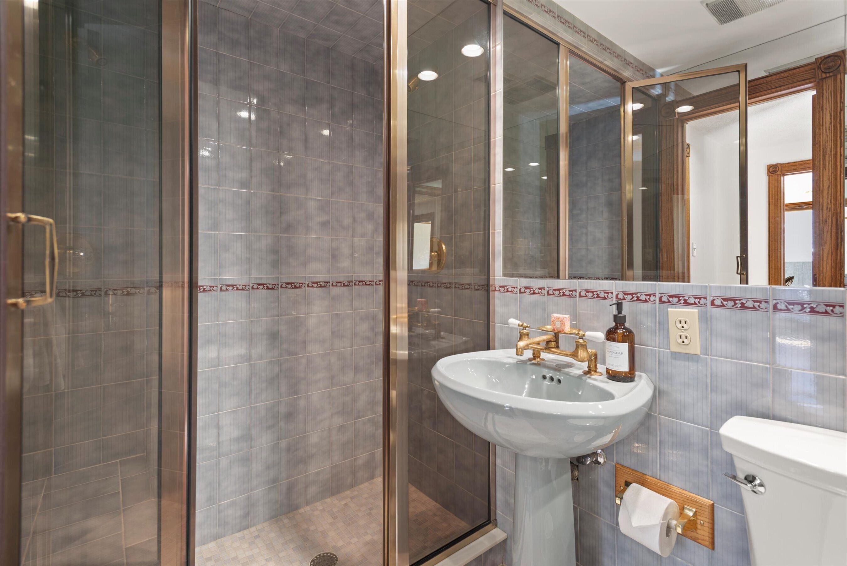 Une salle de bain moderne avec une douche à parois de verre, un lavabo blanc avec des robinets dorés et des toilettes.
