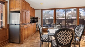 A kitchen with wooden cabinets, a stainless steel refrigerator, and a dining area with patterned chairs and a table. - 2-Bedroom Top Floor View Condo in Downtown Aspen (Aspen)