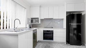 Una cocina moderna con armarios blancos, un lavamanos de acero inoxidable, microondas, lavavajillas y refrigerador negro.