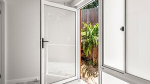 Une porte-fenêtre coulissante donne sur une cour arrière agrémentée d’une clôture en bois et de plantes vertes.