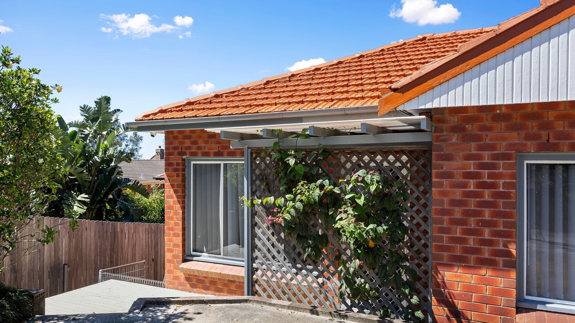 A brick house with a tiled roof, a wooden fence, and a lattice wall with climbing plants.
