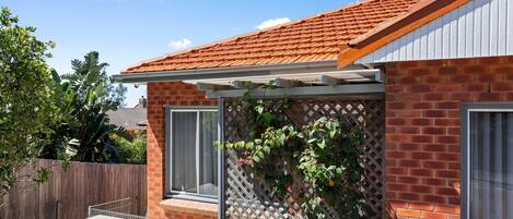 A brick house with a tiled roof, a wooden fence, and a lattice wall with climbing plants.