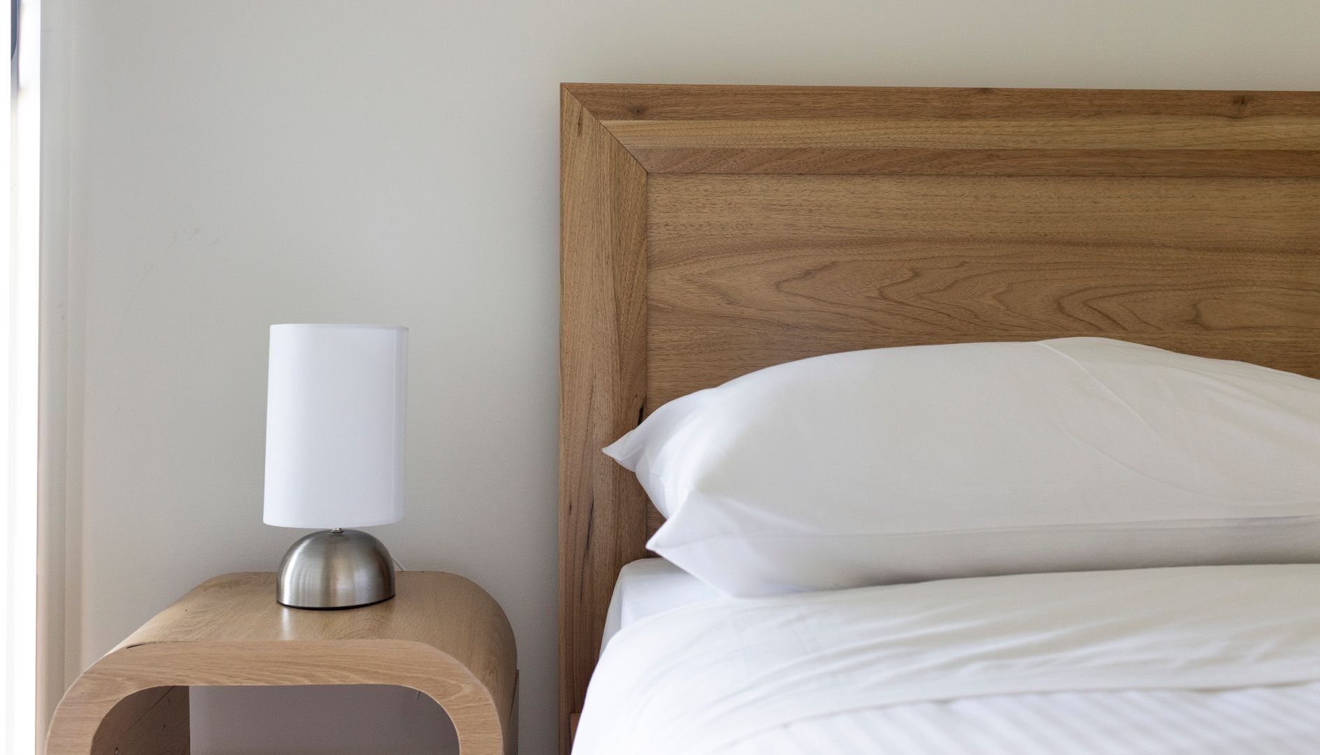 Un lit bien fait, avec du linge de lit blanc et une tête de lit en bois.