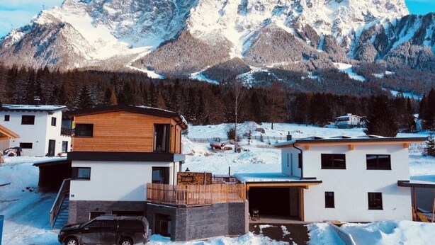 Ein modernes, zweistöckiges Haus mit Holzfassade, einer Garage und einer Auffahrt.