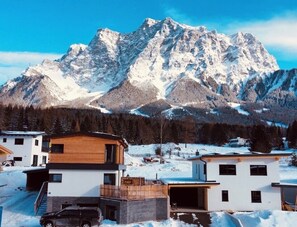 A modern two-story house with a wooden facade, a garage, and a driveway. - Chalet apartment with panoramic mountain views at the foot of the Zugspitze  (Ehrwald)