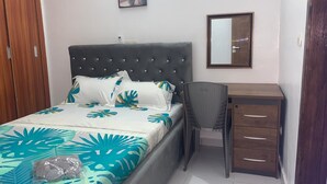 A bedroom with a bed, a desk, a chair, a wardrobe, and a mirror. - The house of happiness (Abidjan)