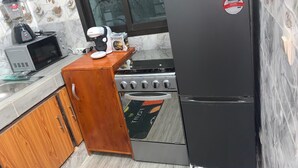 A compact kitchen with a black refrigerator, a stove, a microwave, and a coffee maker. - The house of happiness (Abidjan)