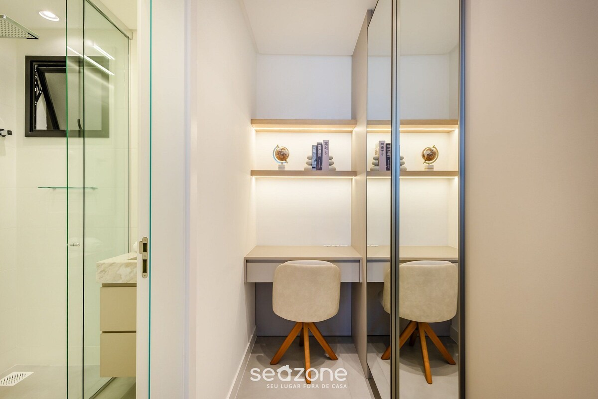A modern bathroom with a glass shower enclosure, a vanity with a marble countertop, and a desk with two chairs.