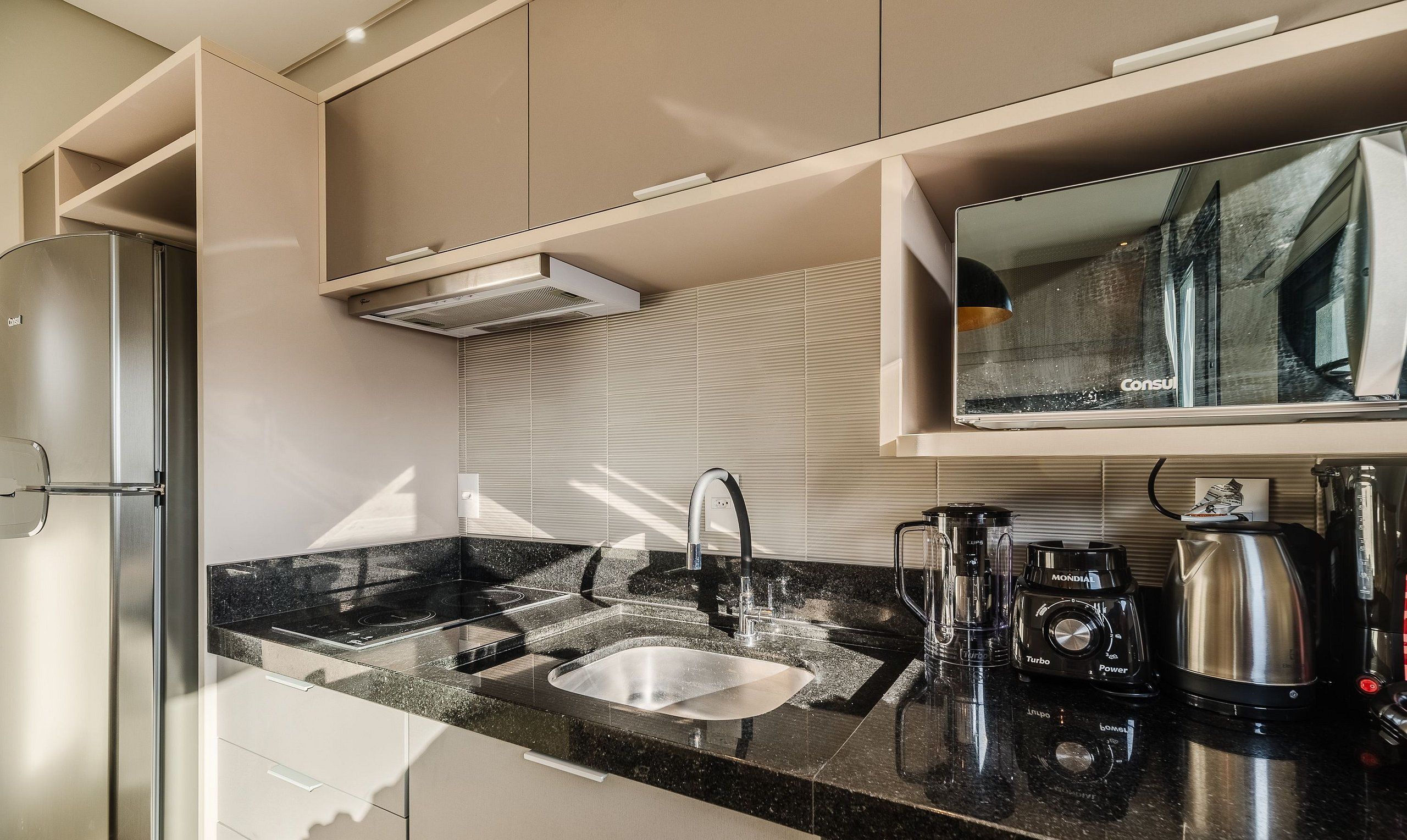 Una cocina moderna con un refrigerador de acero inoxidable, un horno empotrado, un lavamanos con un grifo moderno y diversos electrodomésticos, incluyendo una cafetera y una licuadora.