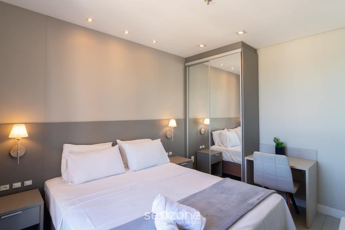 Une chambre d’hôtel moderne avec un grand lit, des tables de chevet, un bureau et un miroir.