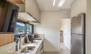 Une cuisine moderne dotée d’un réfrigérateur en acier inoxydable, d’un four encastré et d’une fenêtre donnant sur un paysage verdoyant.
