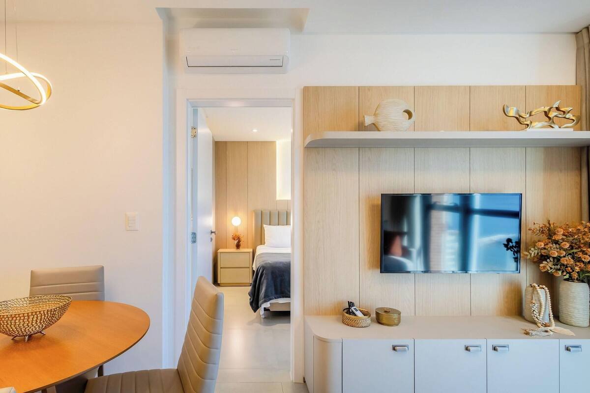 Une chambre d’hôtel moderne dotée d’un coin repas, d’un téléviseur fixé au mur et d’un couloir menant à une autre chambre.