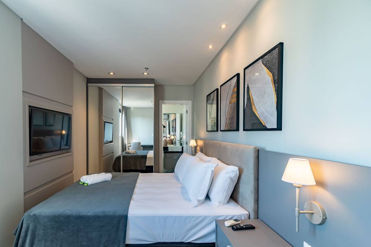 Une chambre d’hôtel moderne équipée d’un lit, d’une table de chevet, d’une lampe, d’œuvres d’art et d’un téléviseur.