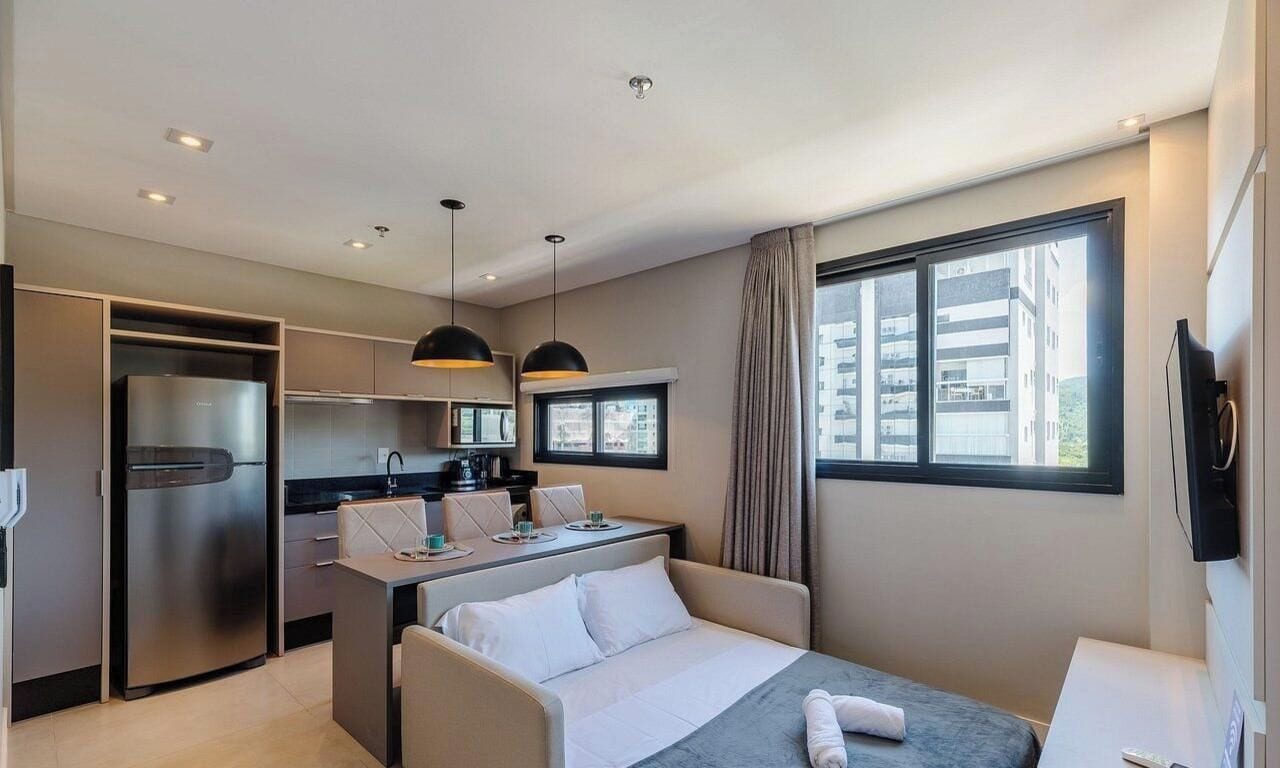 Una habitación de hotel moderna con kitchenette, una cama, un escritorio y un ventanal grande.