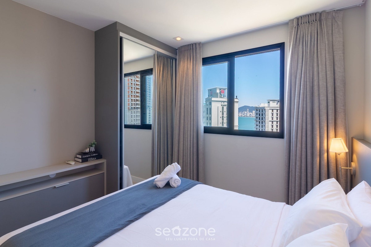 A hotel room with a bed, a nightstand, a mirror, and a window with curtains.