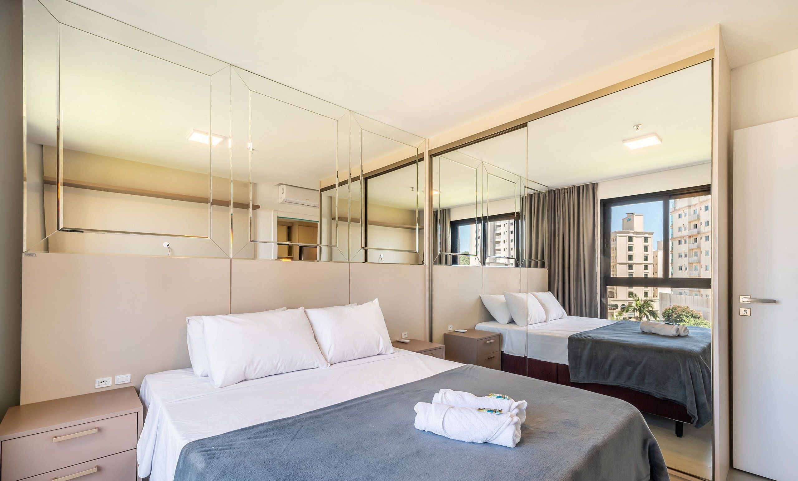 Una habitación de hotel con una cama grande, una cama más pequeña, un escritorio, una silla, un armario y un espejo grande.
