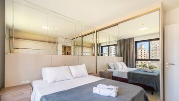 Una habitación de hotel con una cama grande, una cama más pequeña, un escritorio, una silla, un armario y un espejo grande.