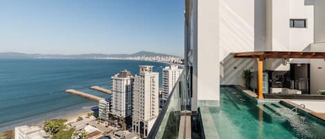 A high-rise building with a pool, overlooking a coastal cityscape.