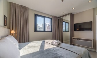 Habitación de hotel con cama, televisión, escritorio y ventana con cortinas.