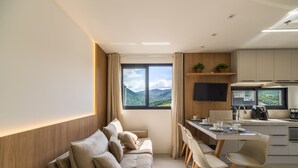 Un salon moderne avec un canapé, une table à manger et des chaises. Il y a également un coin cuisine avec un téléviseur à écran plat et une vue sur les montagnes par la fenêtre.
