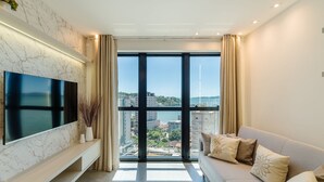 A modern living room with a large TV, a sofa, and a view of a cityscape through large windows. - MHF III Apts Variados a 280m da Praia em Itapema (Itapema)