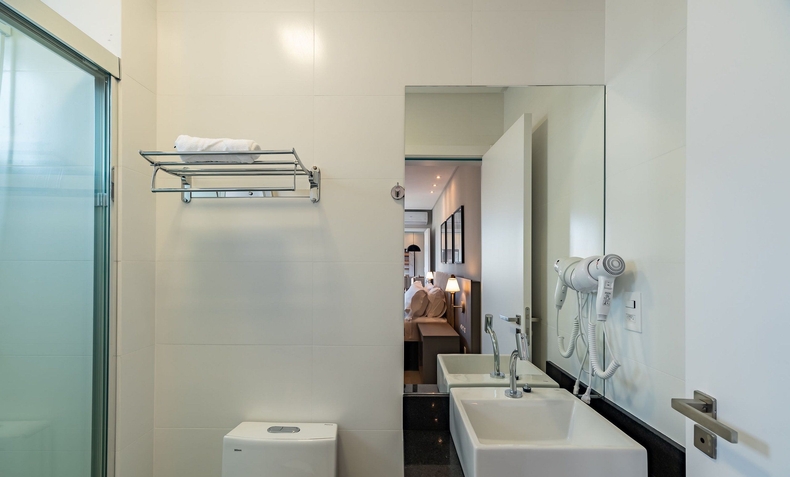 Un baño moderno con cabina de ducha de vidrio, un perchero, un inodoro, un lavabo y un secador de pelo montado en la pared.