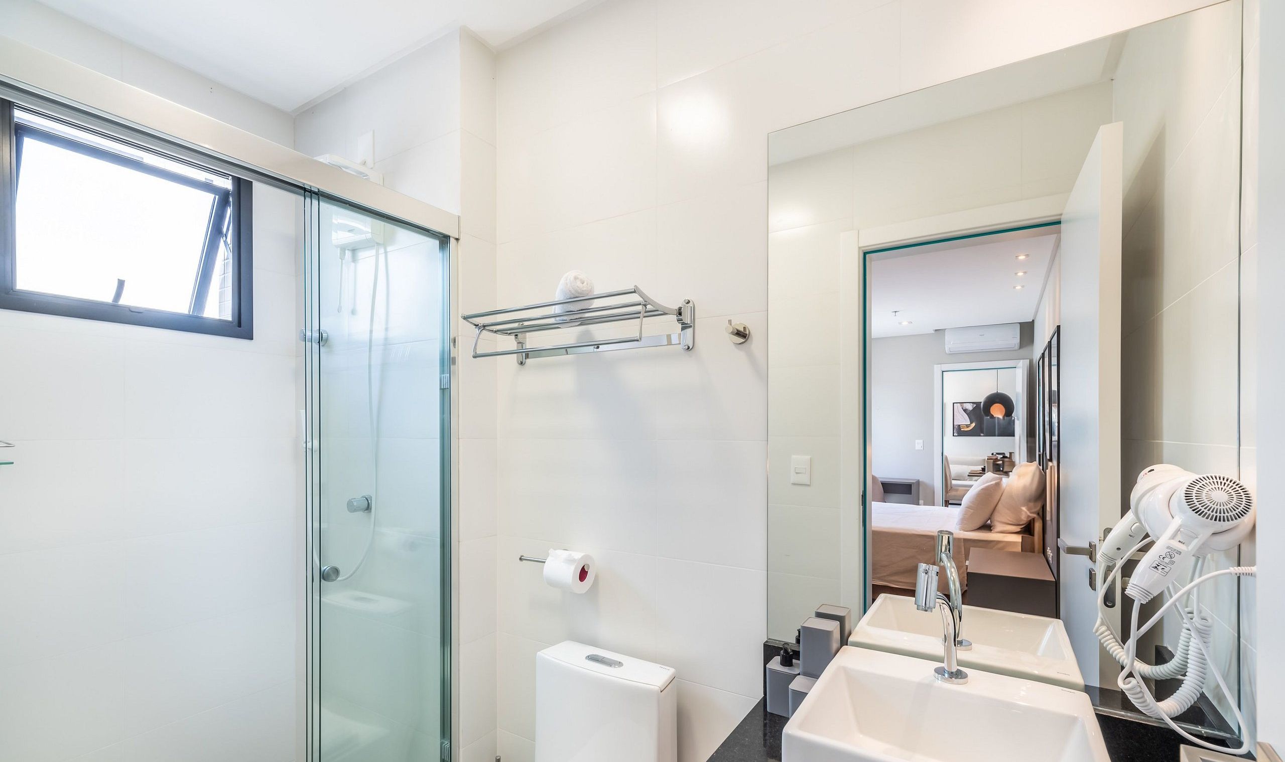 A modern bathroom with a glass shower enclosure, a toilet, a sink with a mirror, and a hairdryer.
