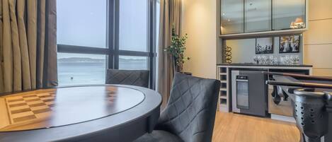 A modern kitchen with a view of the sea, a dining area with a table and chairs, and a bar area with glasses.