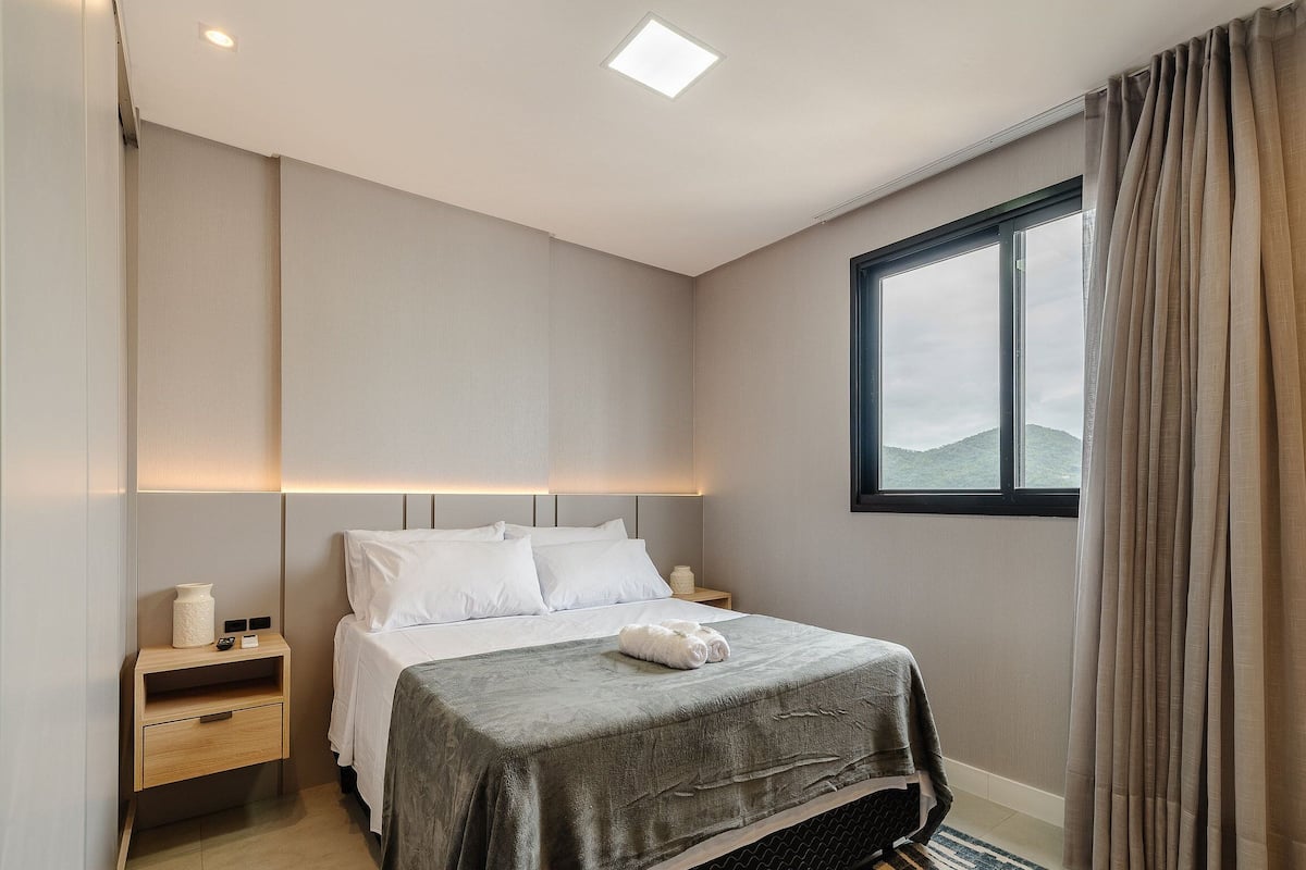 Une chambre d’hôtel avec un lit, des tables de chevet, une fenêtre avec des rideaux et une vue sur une montagne.