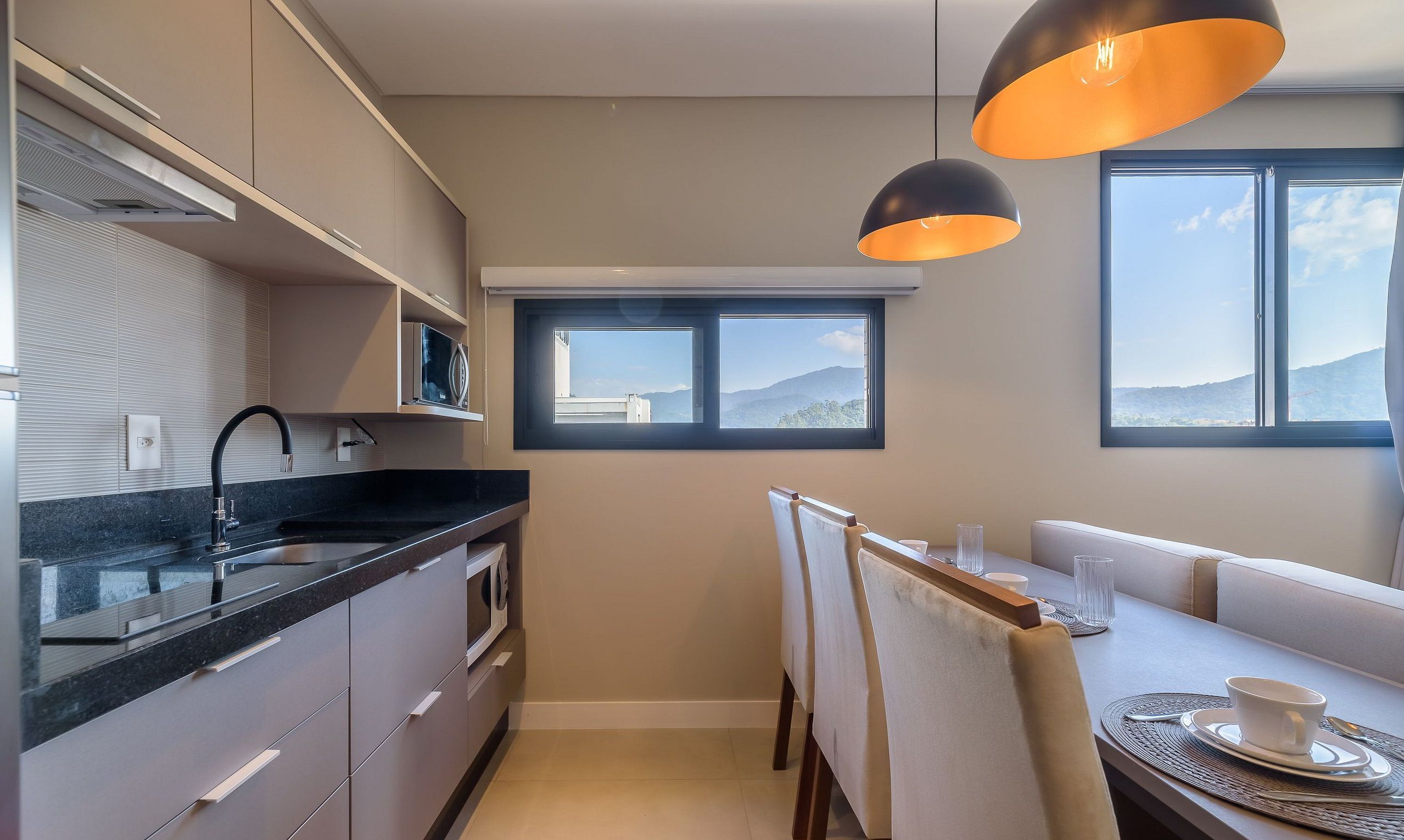 A modern kitchen with a dining area, featuring a large window with a mountain view, pendant lighting, and a built-in oven.