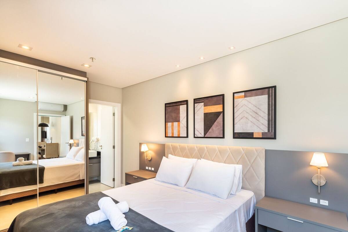 Une chambre d’hôtel avec un lit, des tables de chevet, un miroir et des œuvres d’art accrochées au mur.