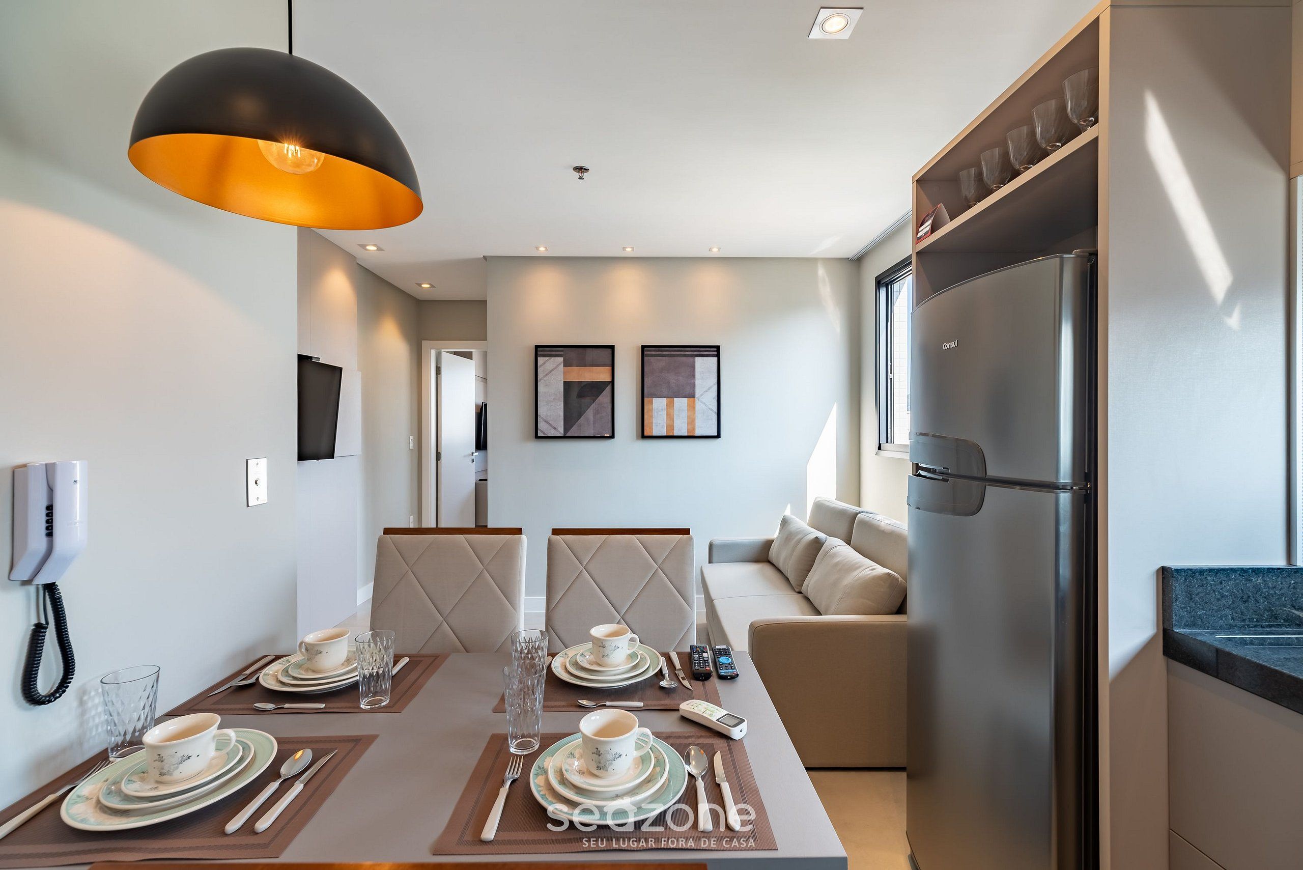 Cozinha moderna com geladeira embutida, área de jantar com mesa posta para dois e um sofá ao fundo.