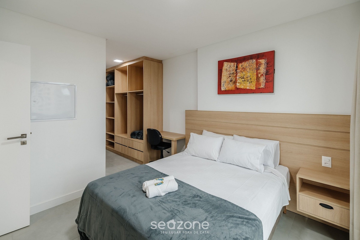 A hotel room with a bed, a desk, a chair, a wardrobe, and a painting on the wall.