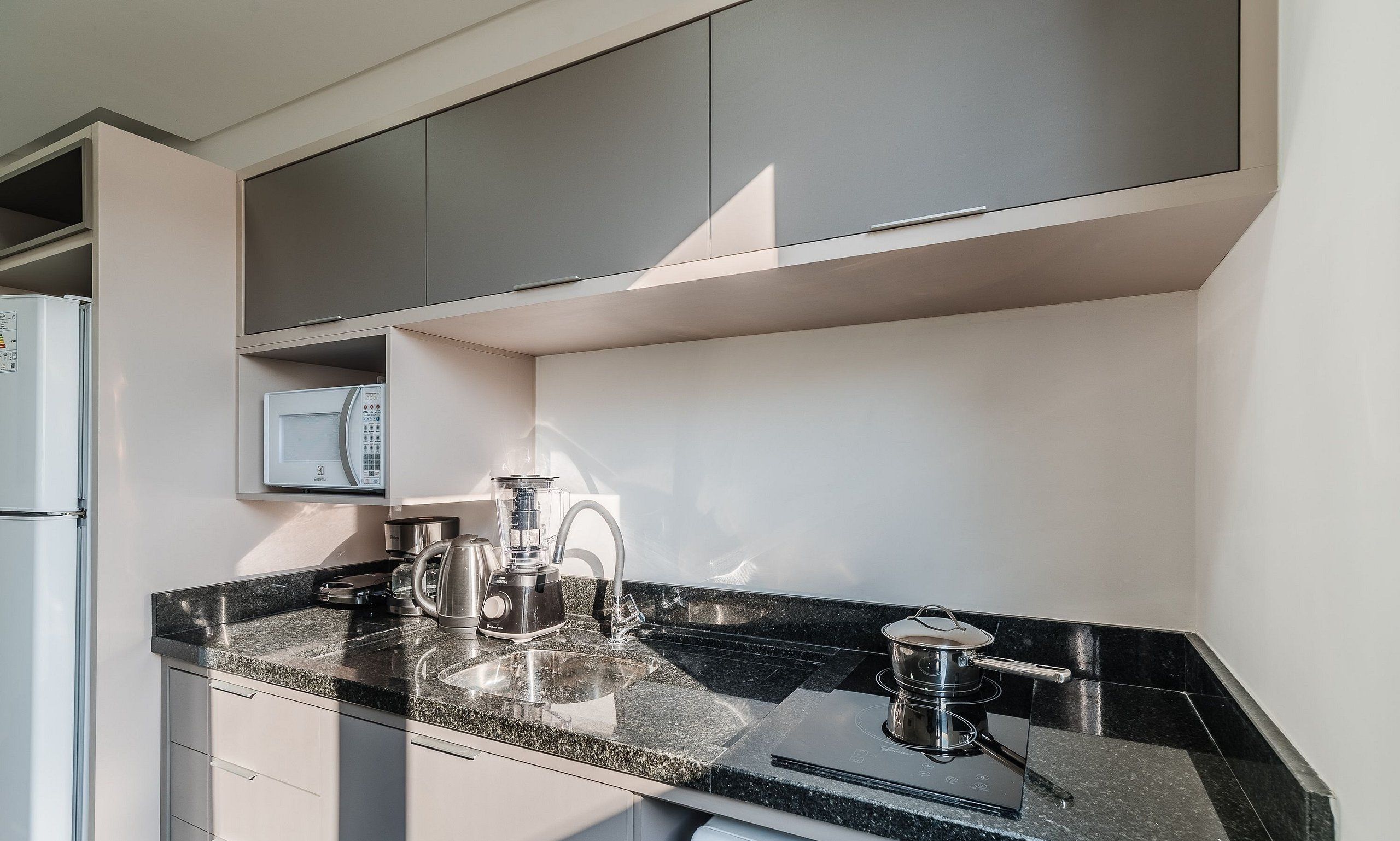Una cocina moderna con encimera de granito, cafetera, hervidor y microondas integrado.