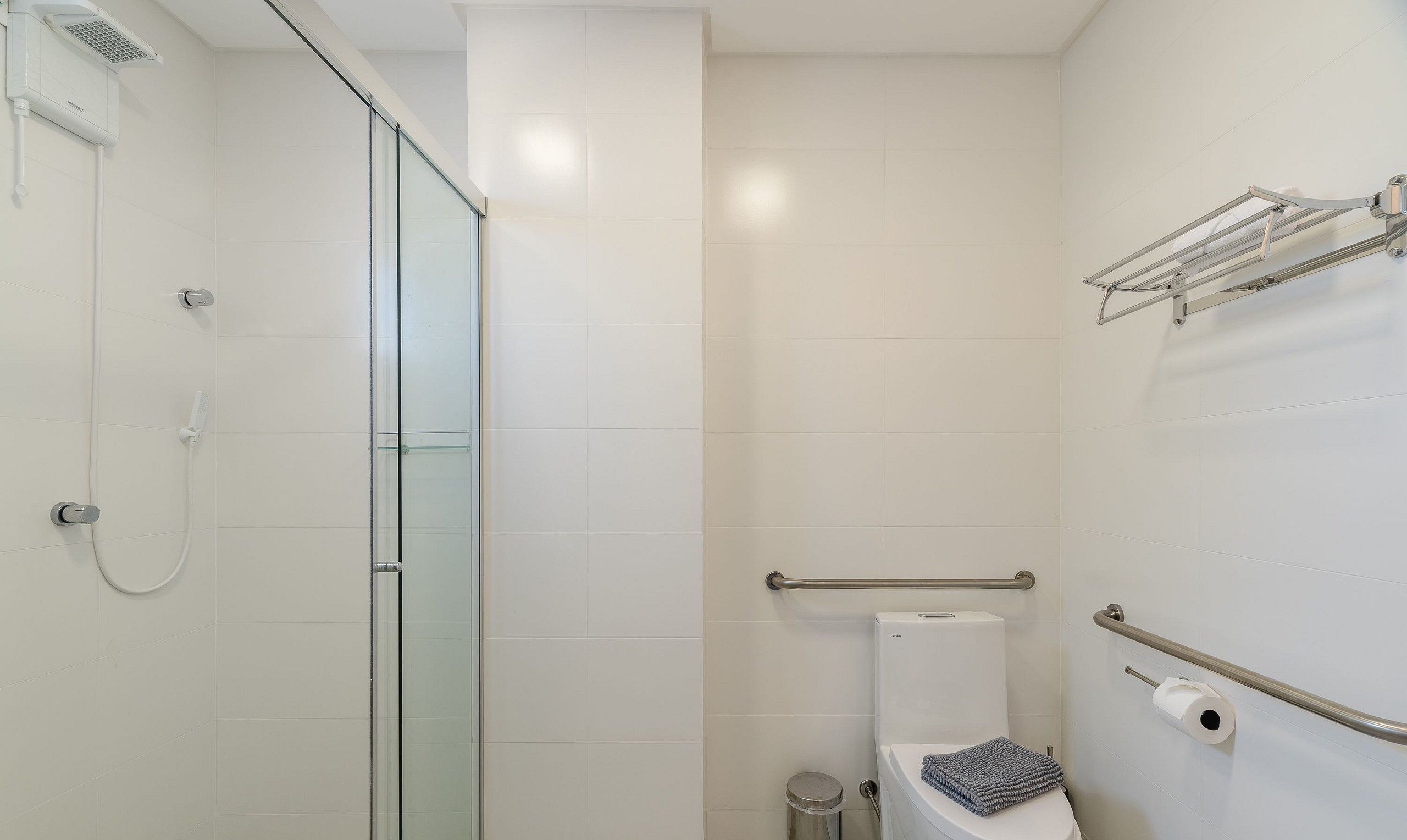 A bathroom with a glass shower enclosure, a toilet, a hand dryer, and a towel rack.